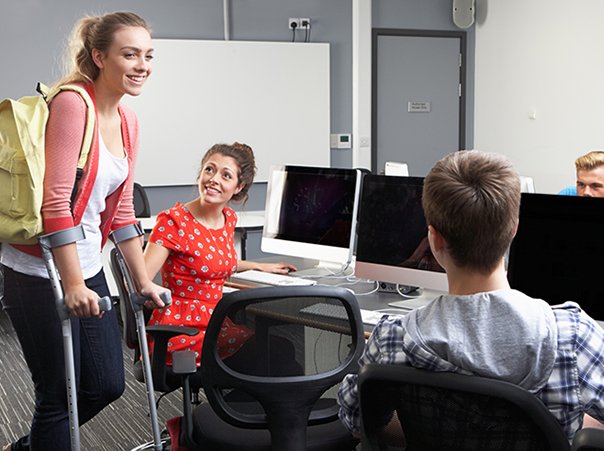 Female Pupil Walking On Crutches In Computer Class Female Pupil Walking On Crutches In Computer Class