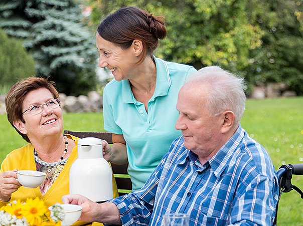 491842784 Caregiver and a senior couple outdoors, sitting at garden table